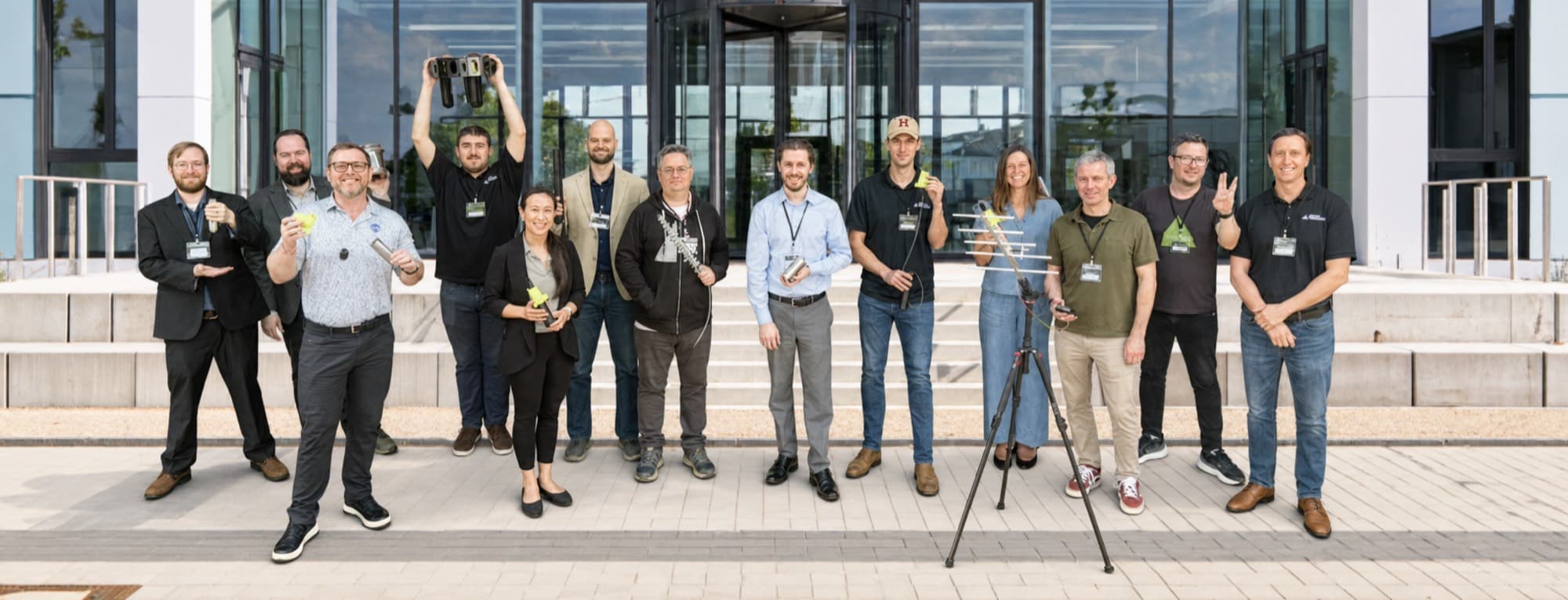 The Ascendant AI team standing together outside a glass office building, several holding drone components and one beside a tripod
